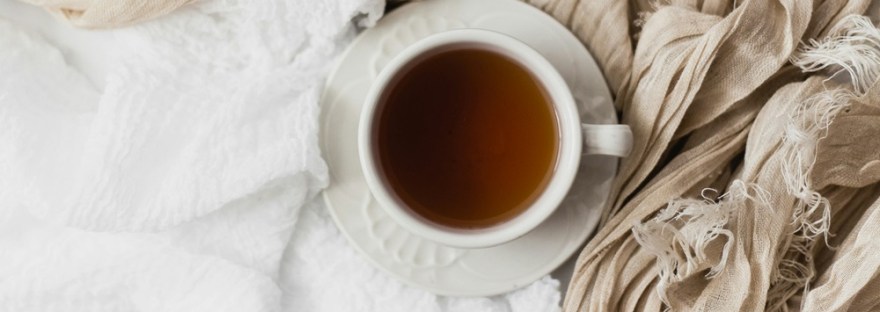 Cup of tea on a white saucer against soft linens